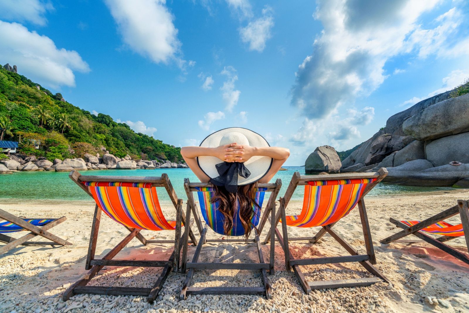 Femme au chapeau assise sur une chaise longue face à une plage tropicale turquoise